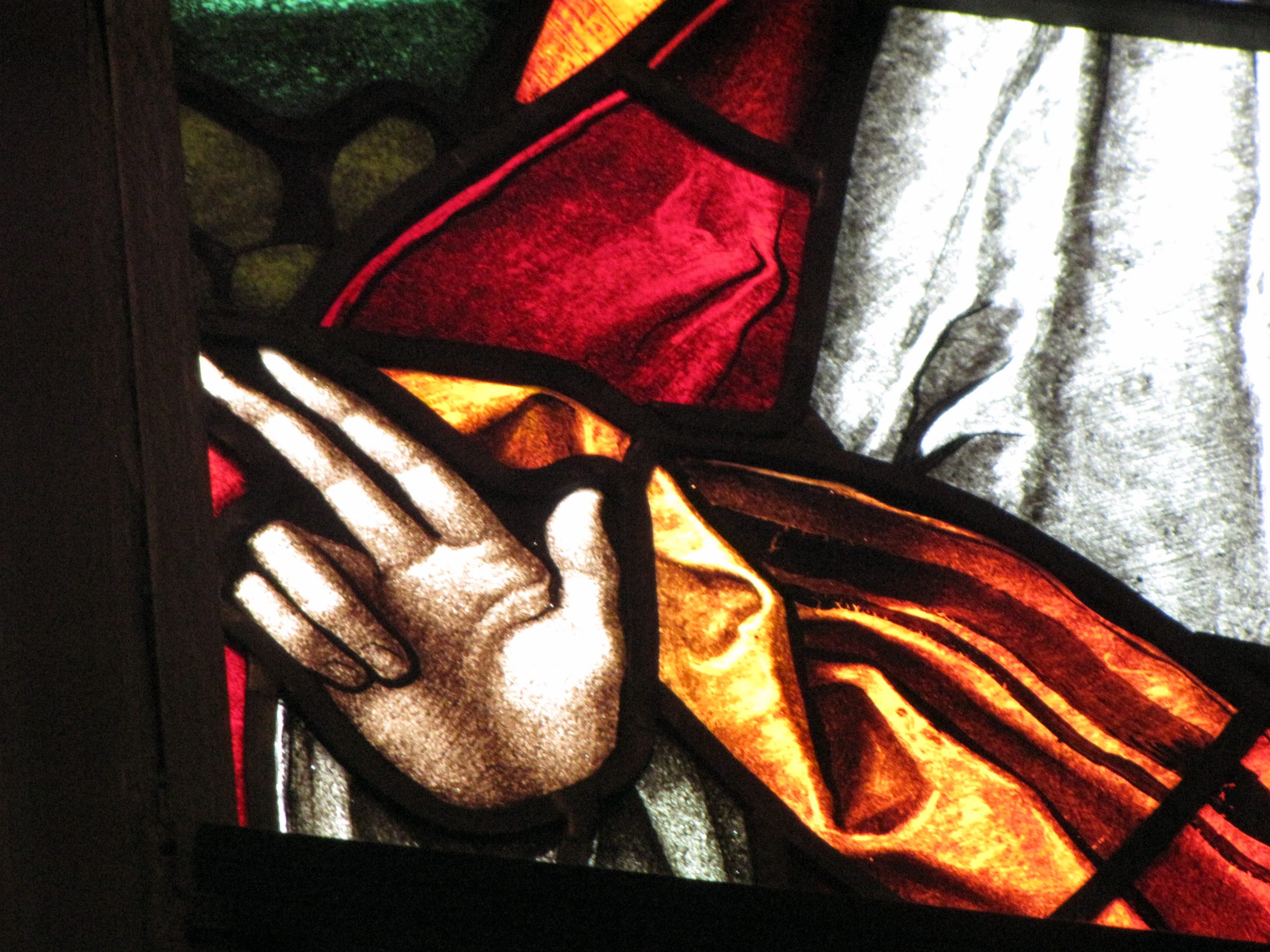 Close detail of a stained glass window in the cathedral: a raised hand and folds of red and gold robe lit from behind