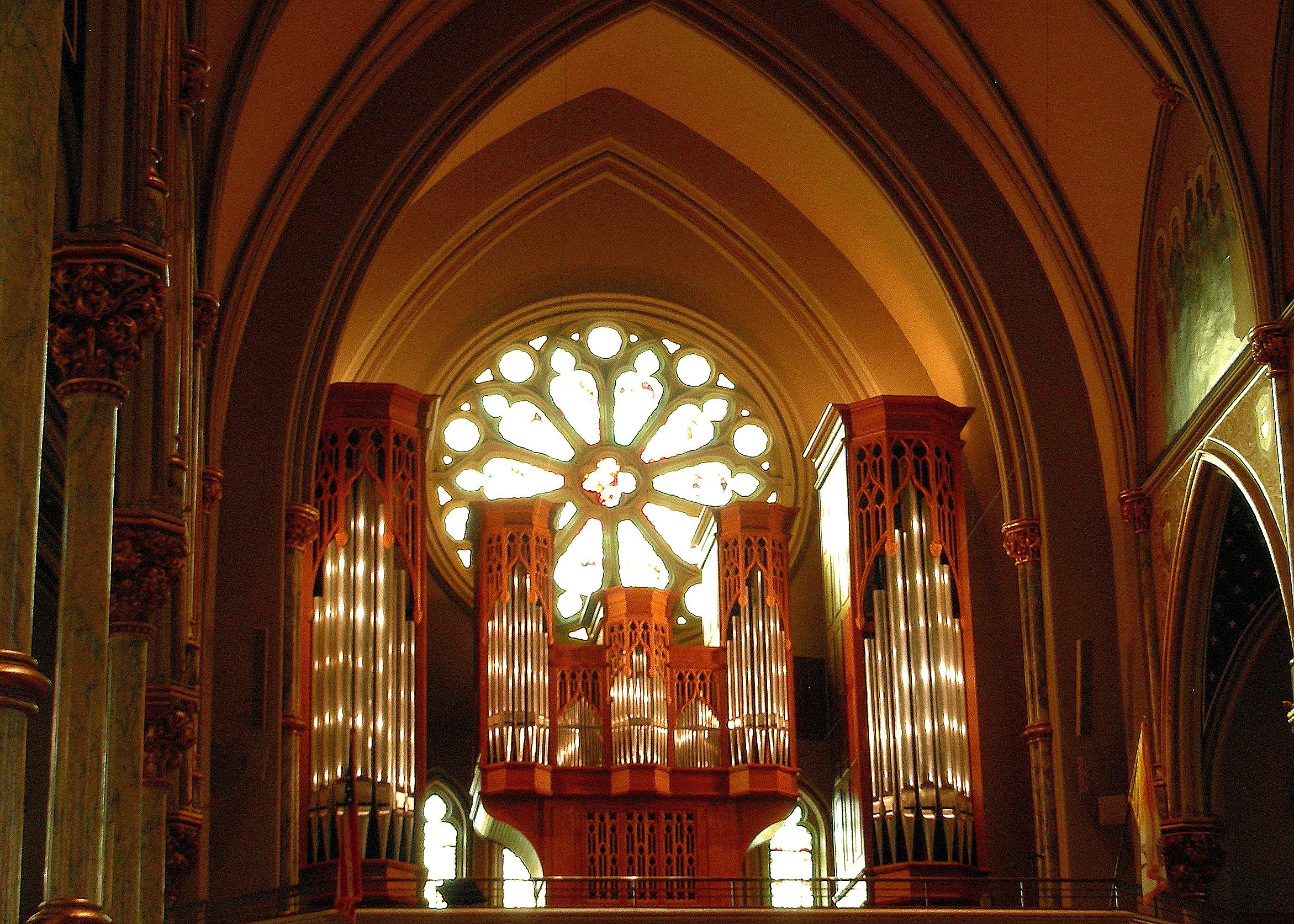 Inside the Cathedral of St. John the Baptist in Savannah: the great rose window glowing above the organ pipes, framed by gold Gothic arches