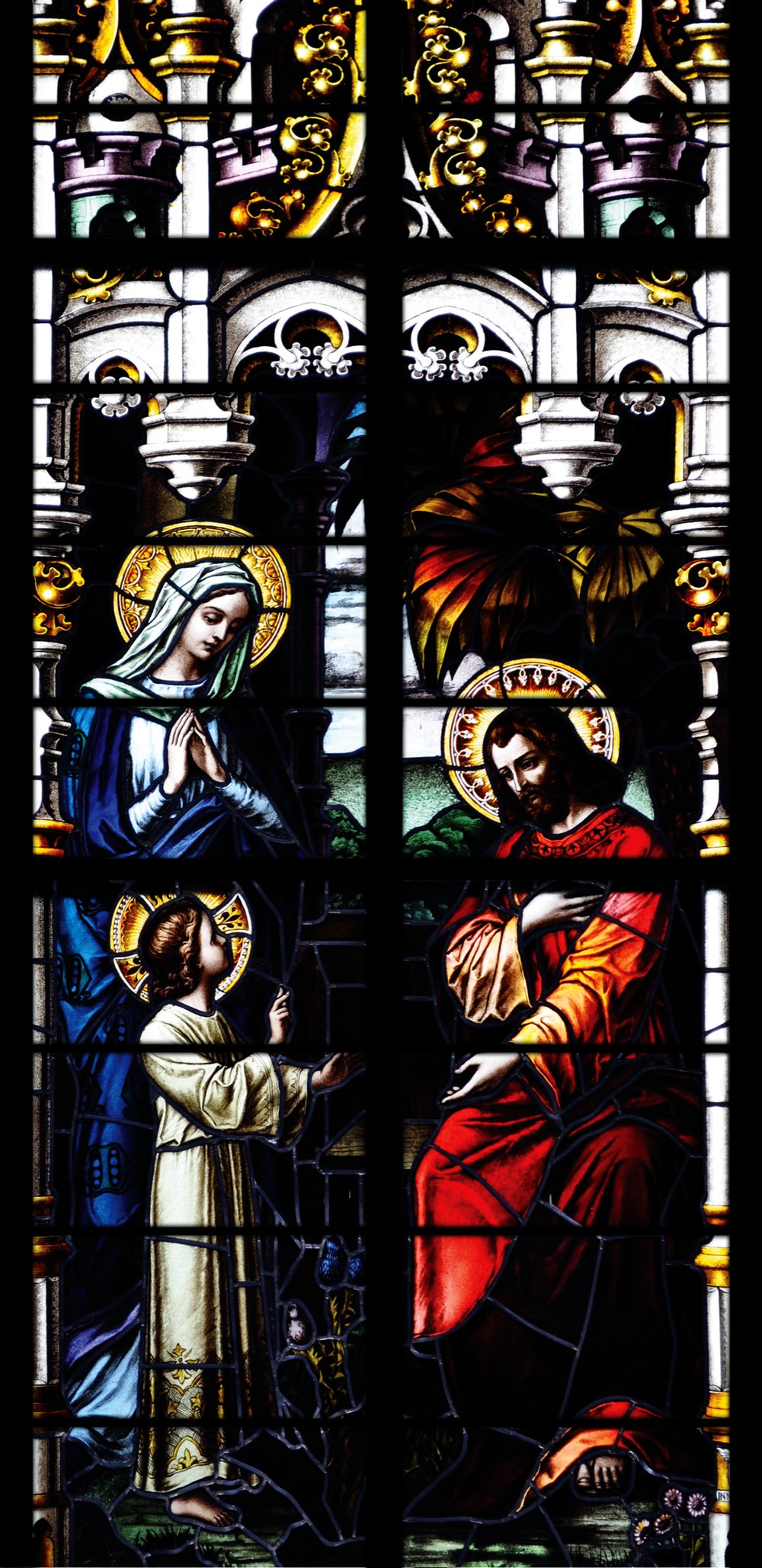 The Holy Family stained glass window: Mary in blue, the young Jesus, and Joseph in red, beneath Gothic tracery